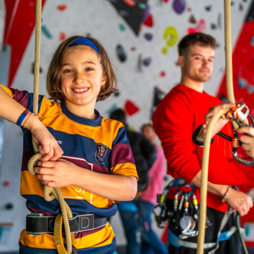 Children practising basic rope skills and belaying techniques at Redpoint Bristol, smiling and working with climbing equipment under staff supervision.