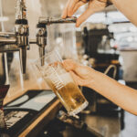 A bartender pouring a golden beer from a draft tap into a branded glass, capturing the flow and foam as the drink fills in a warm, softly lit bar setting.