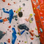 A climber stretches across varied holds on a steep indoor wall, demonstrating balance and technique while ascending a marked route at Redpoint Climbing Centre in Bristol.