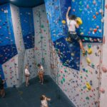 High-angle view of a male climber tackling an overhanging indoor wall while a belayer manages the rope below at Redpoint Climbing Centre in Bristol.